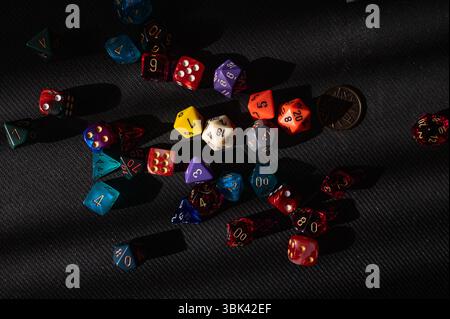 A top-down view of a colorful collection of polyhedral dice scattered chaotically across a black textured background. Stock Photo