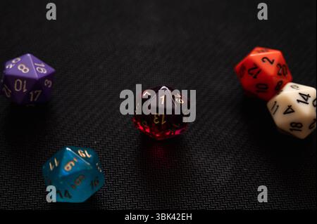 Five colorful 20-sided dice (D20) arranged on a black background. The central red die shows a '1', symbolizing a critical failure Stock Photo