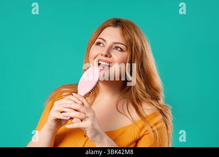 Body positive woman Singing, Dancing With Hair Brush Instead Microphone On Blue  Stock Photo