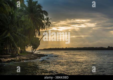 Sunbeams peeking from behind the clouds during sunset at a beach on Isla Batimentos, Bocas del Toro, Panama Stock Photo
