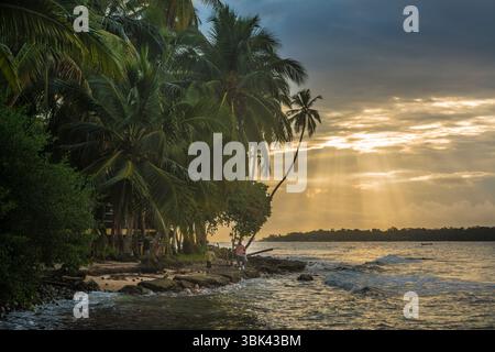Sunbeams peeking from behind the clouds during sunset at a beach on Isla Batimentos, Bocas del Toro, Panama Stock Photo