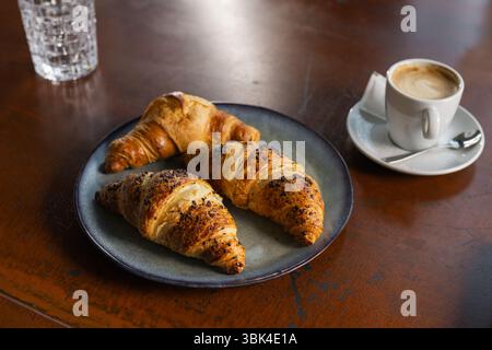 A brunch plate holds freshly baked croissants alongside a small cup of coffee on a wooden table in a warm, inviting cafe. Stock Photo