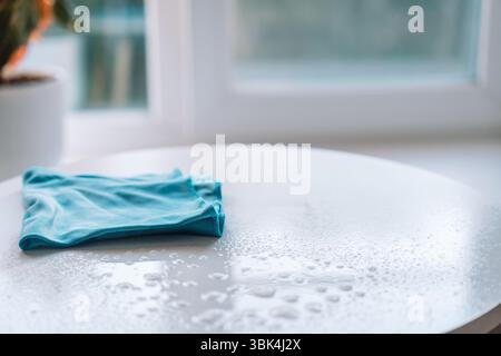 Folded blue microfiber cloth lying on a freshly cleaned white tabletop with water droplets. Stock Photo