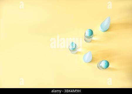 Top view of small cosmetic bottles with blue caps and travel containers arranged diagonally on yellow background. Minimalist hygiene and beauty flat l Stock Photo