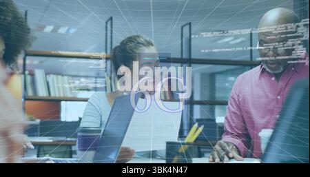 Reviewing woman typing from printed docs on laptop at office desk, with holographic 6G overlay Stock Photo