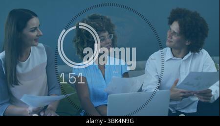 Reviewing three professionals analyzing documents in office lounge, with laptop and data graphic Stock Photo