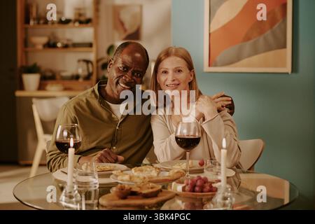 Senior Multiethnic Couple Smiling and Embracing While Enjoying Romantic Dinner Stock Photo