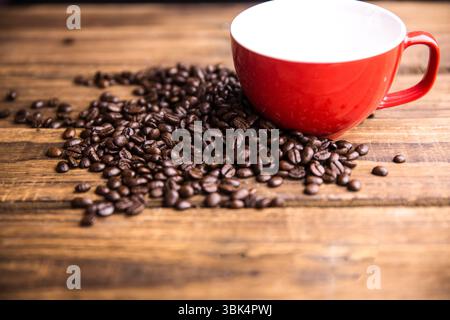 Flat design red ceramic mug is sitting on wooden tabletop with scattered coffee beans in foreground Stock Photo