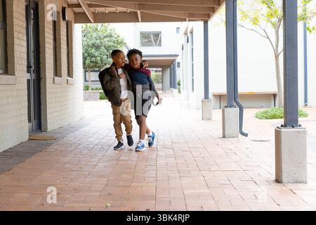 Two diverse boys walking together at school, smiling and enjoying friendship outdoors Stock Photo