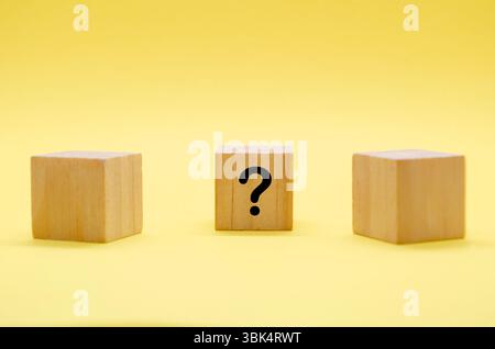 Three light wooden blocks with question marks on pale surface with yellow backdrop. Stock Photo