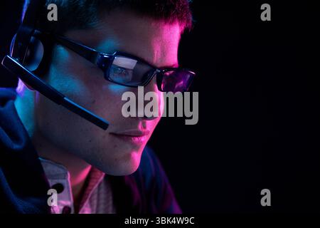 Man wearing eyeglasses and headset with boom microphone focusing on screen in neon room, copy space Stock Photo
