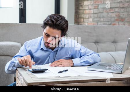 Man reviewing financial documents and using calculator at low wooden coffee table in living room Stock Photo