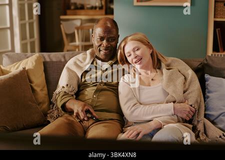 Senior Multiethnic Couple Relaxing Together on Sofa and Watching Television Stock Photo