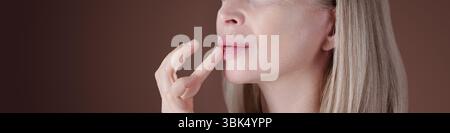 Caucasian woman gently touching her lips with her fingers. Long straight blonde hair cascading down her shoulders Stock Photo