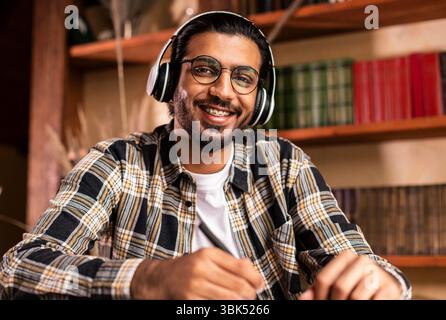 Portrait Of Happy Indian Student Sitting At Desk In Library Stock Photo