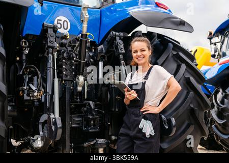 Female agricultural machinery technician using digital tablet to inspect tractor Stock Photo