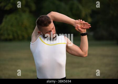 A young fit man doing stretching exercises before running or workout in a park. Active lifestyle, fitness and outdoor exercise concept. Stock Photo