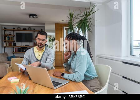 Two business professionals working together in an office reviewing documents and analyzing ideas using a laptop during a collaborative meeting focused Stock Photo