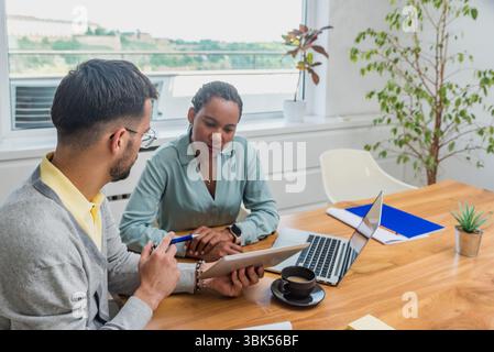 Two business professionals working together in an office reviewing documents and analyzing ideas using a laptop during a collaborative meeting focused Stock Photo