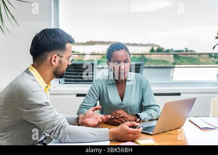 Two business professionals working together in an office reviewing documents and analyzing ideas using a laptop during a collaborative meeting focused Stock Photo