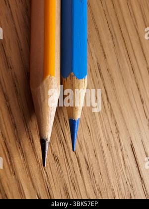 Two sharpened wooden pencils, one yellow and one blue, resting on a wooden table. A close-up detail of everyday stationery essentials for drawing Stock Photo