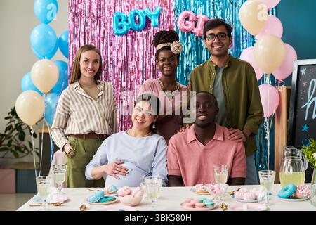 Group of young adult and middle aged multiethnic men and women smiling and posing at gender reveal party, pregnant Caucasian woman sitting in front Stock Photo
