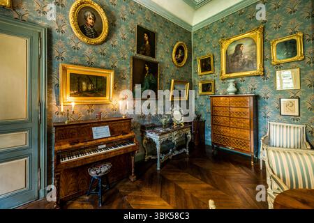 The Pleyel piano stands in the salon of the George Sand House (Maison de George Sand) on Place Sainte-Anne in Nohant, municipality of Nohant-Vic, in the Berry, Indre department, Centre-Val de Loire, France. Candles burn in two candlesticks on the piano, with an upholstered stool in front of it. Beside it stand a marble console table with curved legs and a mirror, and on the right a chest of drawers with inlay work. Portraits in gilded frames hang on the blue floral wallpaper. Portraits of George Sand, her ancestors and descendants hang in the salon. The evening continued there with games and m Stock Photo