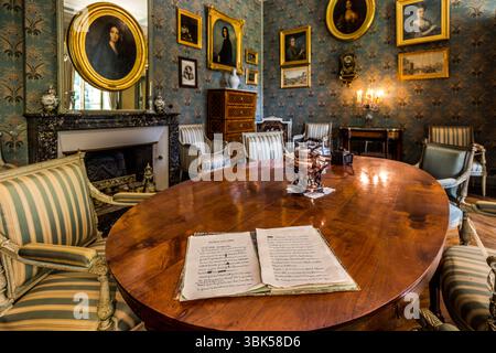 Handwritten sheets lie open on the oval table in the salon of the George Sand House (Maison de George Sand) on Place Sainte-Anne in Nohant, municipality of Nohant-Vic, in the Berry, Indre department, Centre-Val de Loire, France. A small copper kettle on a stand is placed beside them. Striped Louis XVI armchairs stand around the table. Portraits of her ancestors and descendants hang on blue floral wallpaper behind it. Above the fireplace hangs the famous portrait of George Sand by Auguste Charpentier from 1838. The salon displays a copy, and the original is in the Musée de la Vie romantique in  Stock Photo