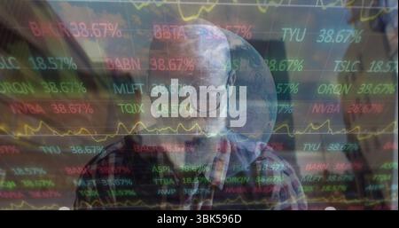 Contemplating man wearing plaid shirt viewing charts in study with holographic globe, stock tickers Stock Photo