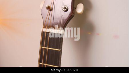 Showing acoustic guitar headstock leaning against wall, with tuning pegs, strings and lens flare Stock Photo