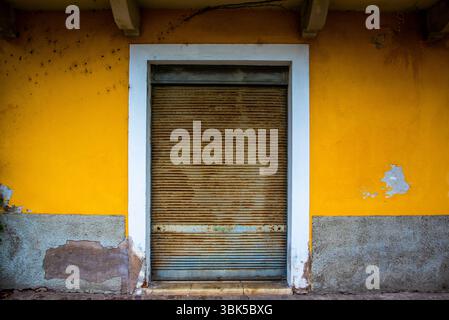 ancient rusty closed shutter set in an ocher yellow wall in Riva del Garda, Trento, Italy Stock Photo