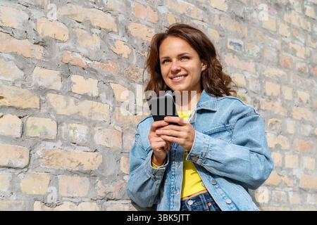 Young urban woman using smartphone near the brick wall Stock Photo