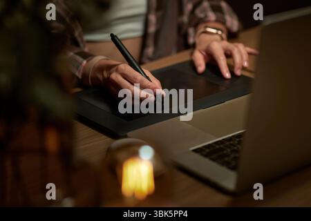female hands with graphic tablet retouching photo on laptop computer at night Stock Photo