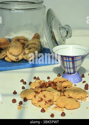 Chocolate chip cookies spilled beside a ceramic cup and glass jar, Stock Photo
