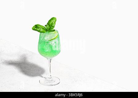 Green Parrot Cocktail on white background, copy space. Gin Basil Smash drink with ice cubes. Refreshing summer basil mocktail. Stock Photo