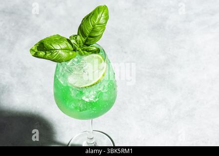 Green Parrot Cocktail on gray background, copy space. Gin Basil Smash drink with ice cubes. Refreshing summer basil mocktail. Stock Photo