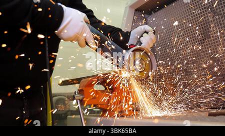 Metalworker using angle grinder with flying sparks. Close-up of a worker cutting metal with an angle grinder, producing bright flying sparks in a Stock Photo