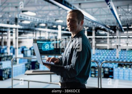 Portrait of smiling engineer in AI data center monitoring error logs for debugging processes. Cheerful employee in server farm reviewing code for artificial intelligence based automation scripts Stock Photo