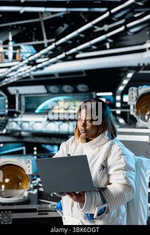 Astronaut using laptop to confirm suit integrity and update flight log. Orbital station crew member testing gear during routine equipment check using notebook, verifying navigation coordinates Stock Photo