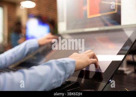 Closeup of creative professional using touchscreen monitor on their office desk, developing 3d videogame scenes. Selective focus on hands of graphic expert utilizing digital screen for illustrations. Stock Photo