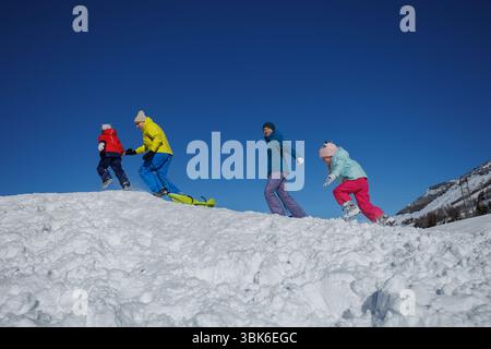 Family of four enjoys a fun snow day, sledding under blue skies Stock Photo