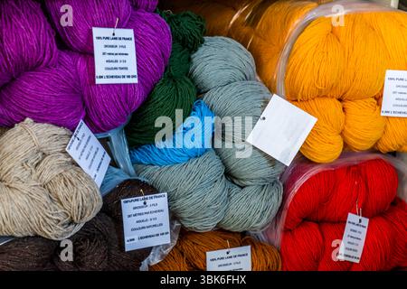Skeins of pure new wool in many shades lie for sale at the Terrade spinning mill (Filature Terrade) on Rue de la Papeterie in Felletin near Aubusson, Creuse, Nouvelle-Aquitaine, France. Purple, dark green, turquoise, grey-green, amber, red, beige, brown and ochre skeins lie partly in plastic bags. The labels bear the inscription "100 % pure laine de France". In English: "100 % pure wool from France". They state a thickness of three ply, 267 metres per 100-gram skein, knitting needles of size 3 to 3.5 and the prices for dyed wool (6.50 euros) and natural-coloured wool (4.50 euros). Hand-dyed pu Stock Photo