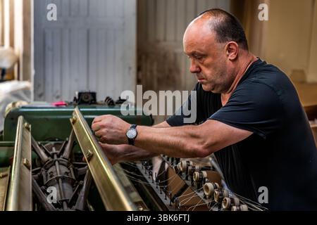 Employees of the Terrade spinning mill (Filature Terrade) working on an old textile machine. The spinning mill is one of the last traditional production sites for textile crafts in France and cultivates knowledge that is directly linked to regional identity and the famous Aubusson tapestry. Rue de la Papeterie, Felletin, Nouvelle-Aquitaine, France Stock Photo