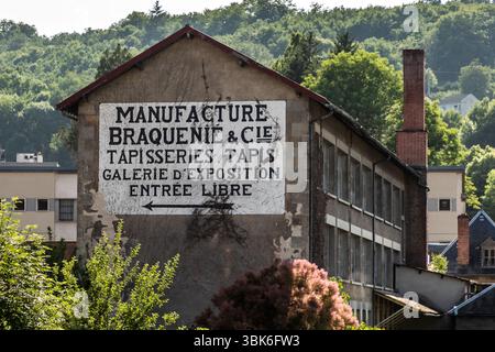 House wall in Aubusson with an old sign advertising an exhibition of tapestries. The history of tapestry in Aubusson dates back to the 15th century. Originally, Aubusson was known for producing tapestries, not carpets for walking on. Over the centuries, the knowledge was passed down in small workshops, and the weavers gained a reputation for their craftsmanship. Pont de la Terrade, Aubusson, Nouvelle-Aquitaine, France Stock Photo