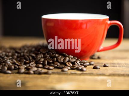 Flat design is showing bright red ceramic coffee cup on wood counter with medium roast beans Stock Photo