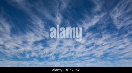 Wispy cirrus clouds are drifting across deep blue sky in flat design, illustrating airy expanse Stock Photo