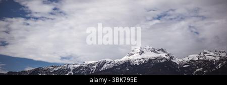 Snow-covered mountain range is rising sharply under cloudy sky with blue patches in flat design Stock Photo