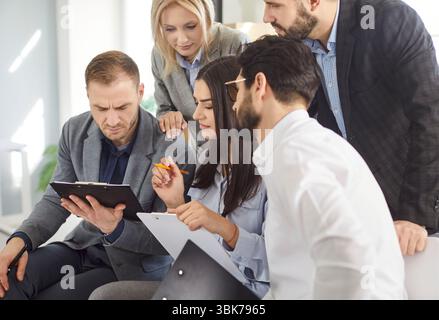 Focused business team gathered around tablet with documents discussing strategy and analyzing data. Stock Photo