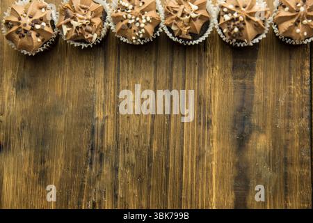 Vector showing row of 7 chocolate cupcakes in liners on wooden table with swirl frosting, sprinkles Stock Photo