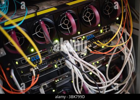 Showing closeup rack of switches and routers, featuring cooling fans with LED lights and cables Stock Photo